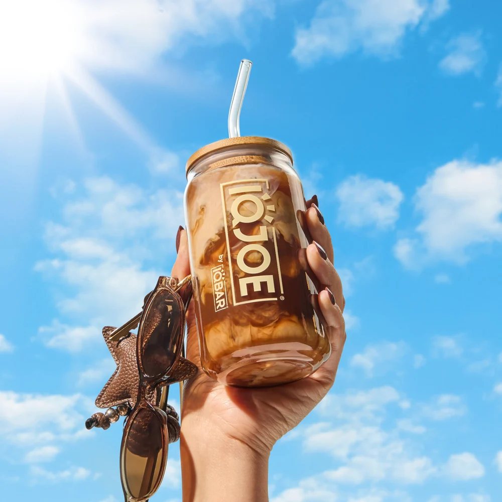 Hand holding an iced IQJOE coffee up to a bright blue sky
