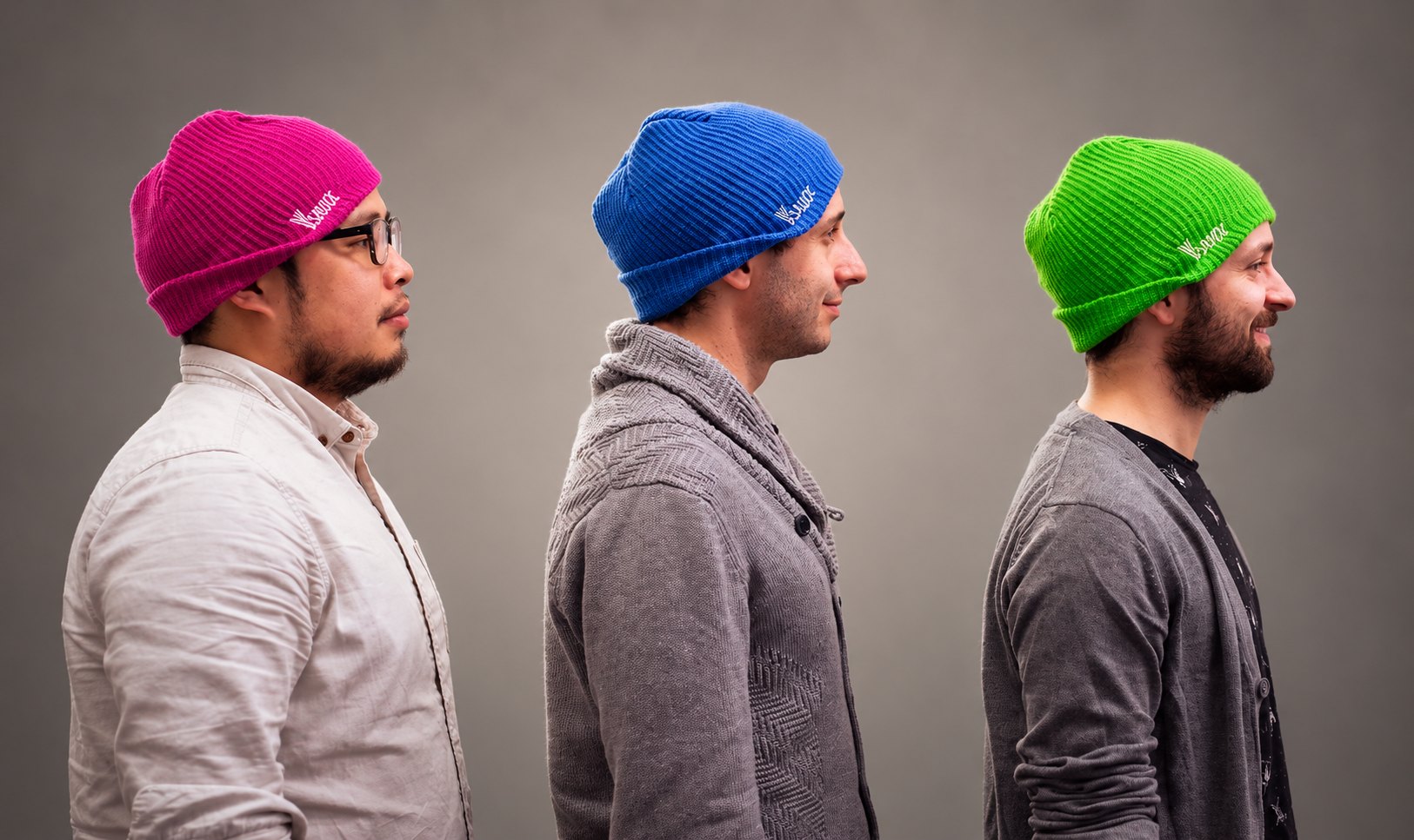 The Vsauce hosts wearing pink, blue, and green Vsauce beanies