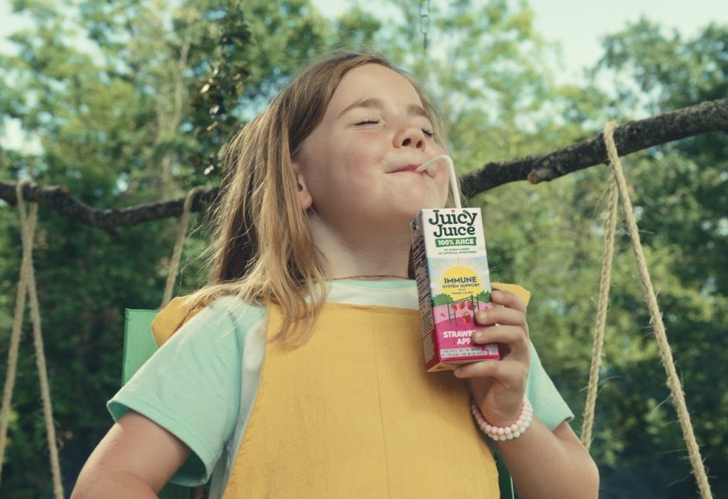 A girl on a tree swing sips a Juicy Juice Immune System Support juice box, eyes closed in bliss