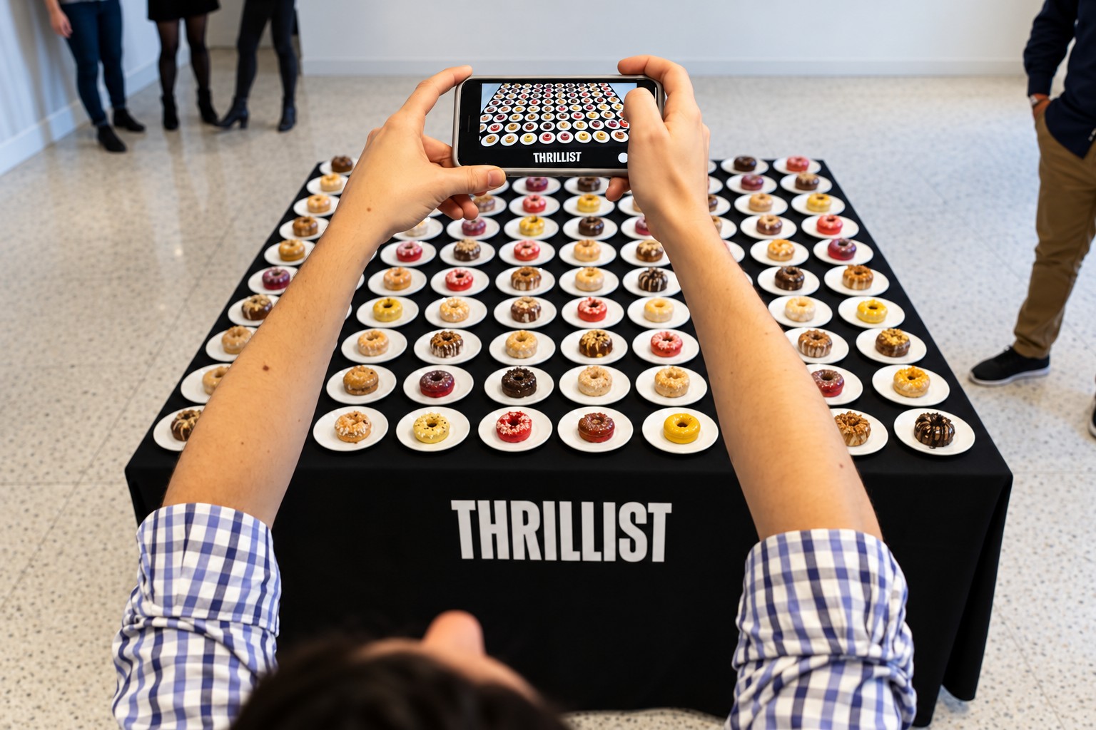 A guest photographing a grid of glazed donuts on a Thrillist-branded table