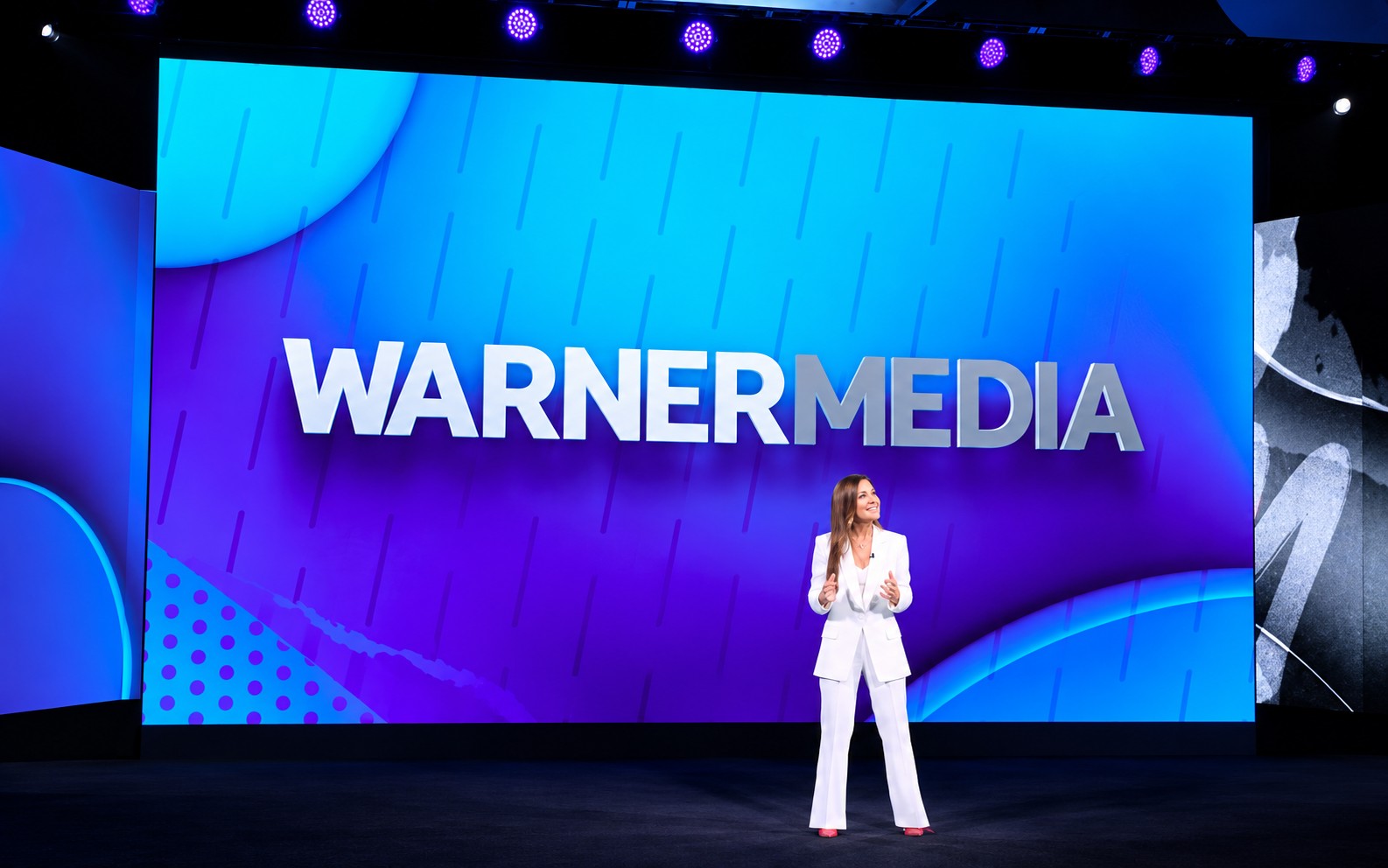 A WarnerMedia executive presenting on stage in front of a giant WarnerMedia screen