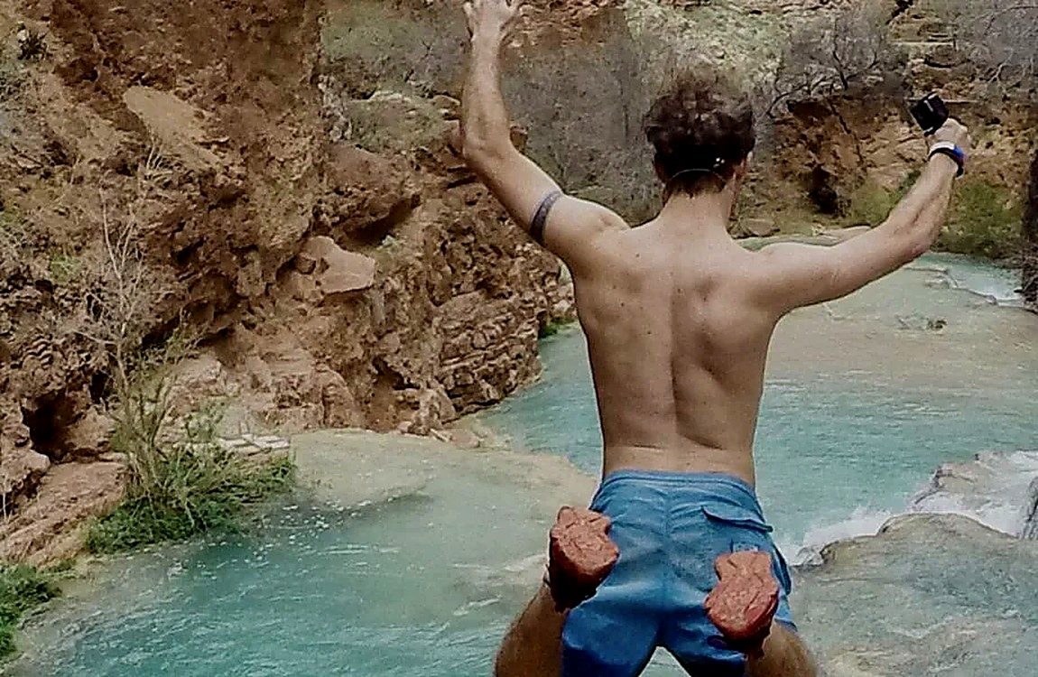 A man cliff-jumping into a turquoise swimming hole