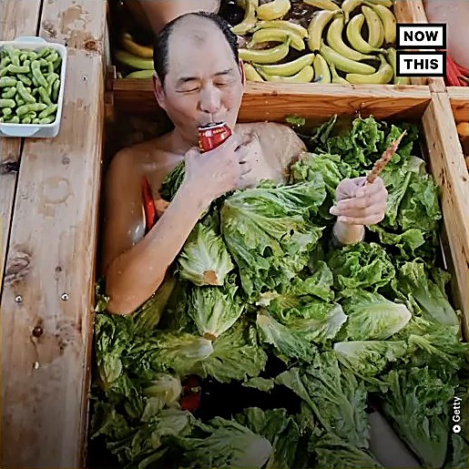 A man soaking in a giant hot pot surrounded by vegetables